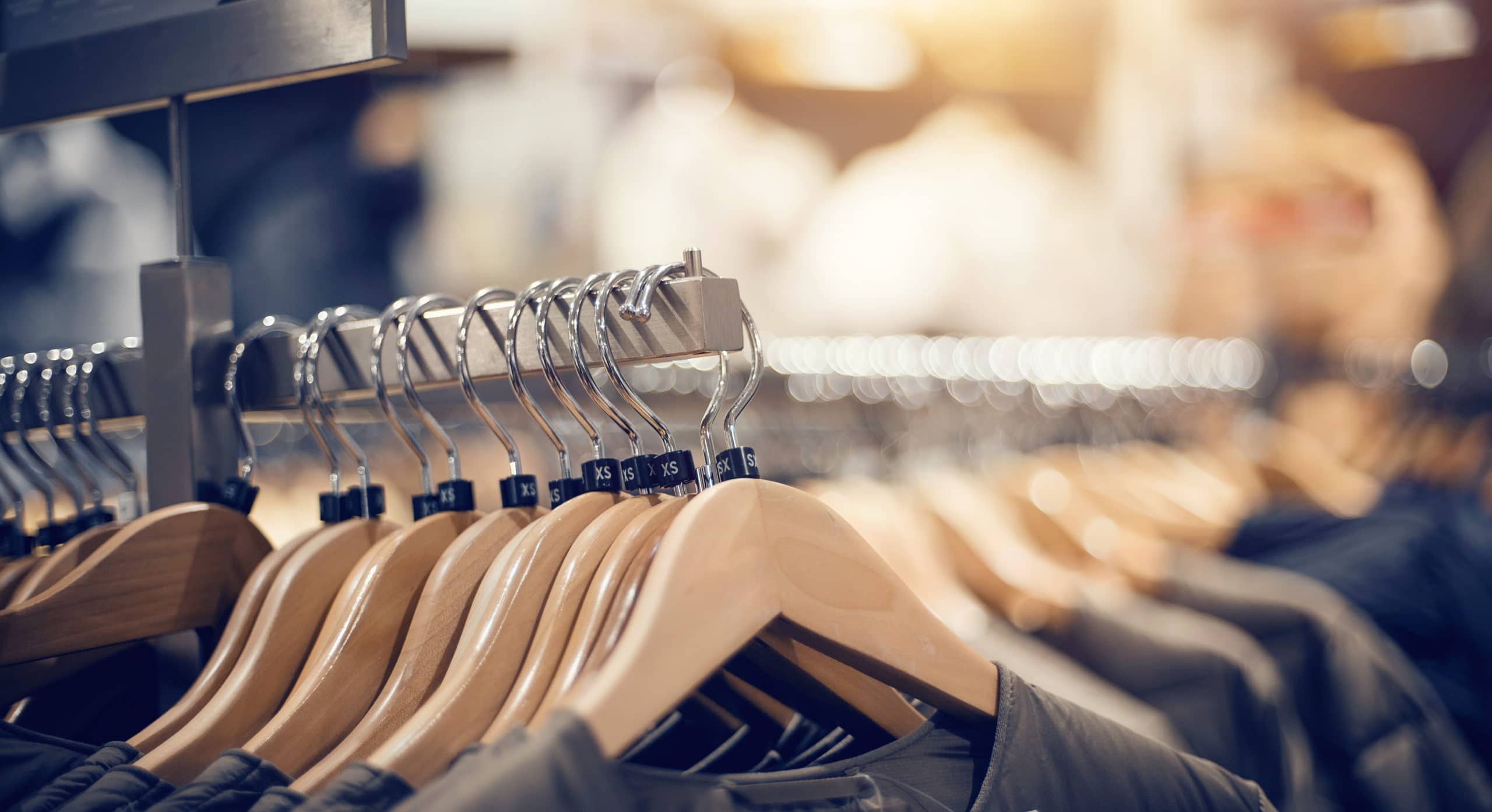 Hangers with clothes on the rail in the store. Shopping in store. Clothes on hangers in shop for sale. Blur background. Fashionable clothes in a boutique. Various clothing on market.